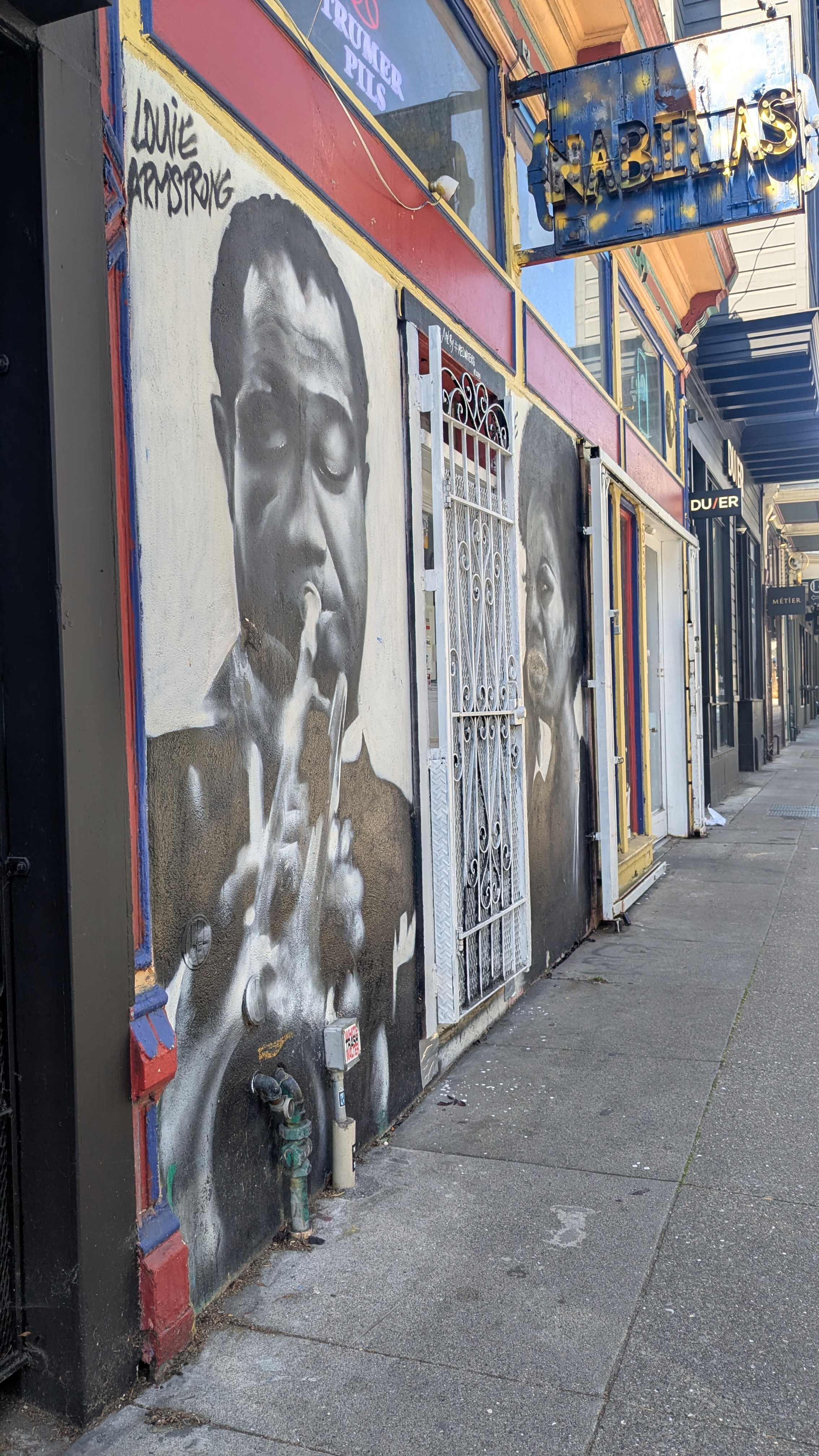 Murals of Louis Armstrong and Ella Fitzgerald on a building, with a DUER storefront down the block