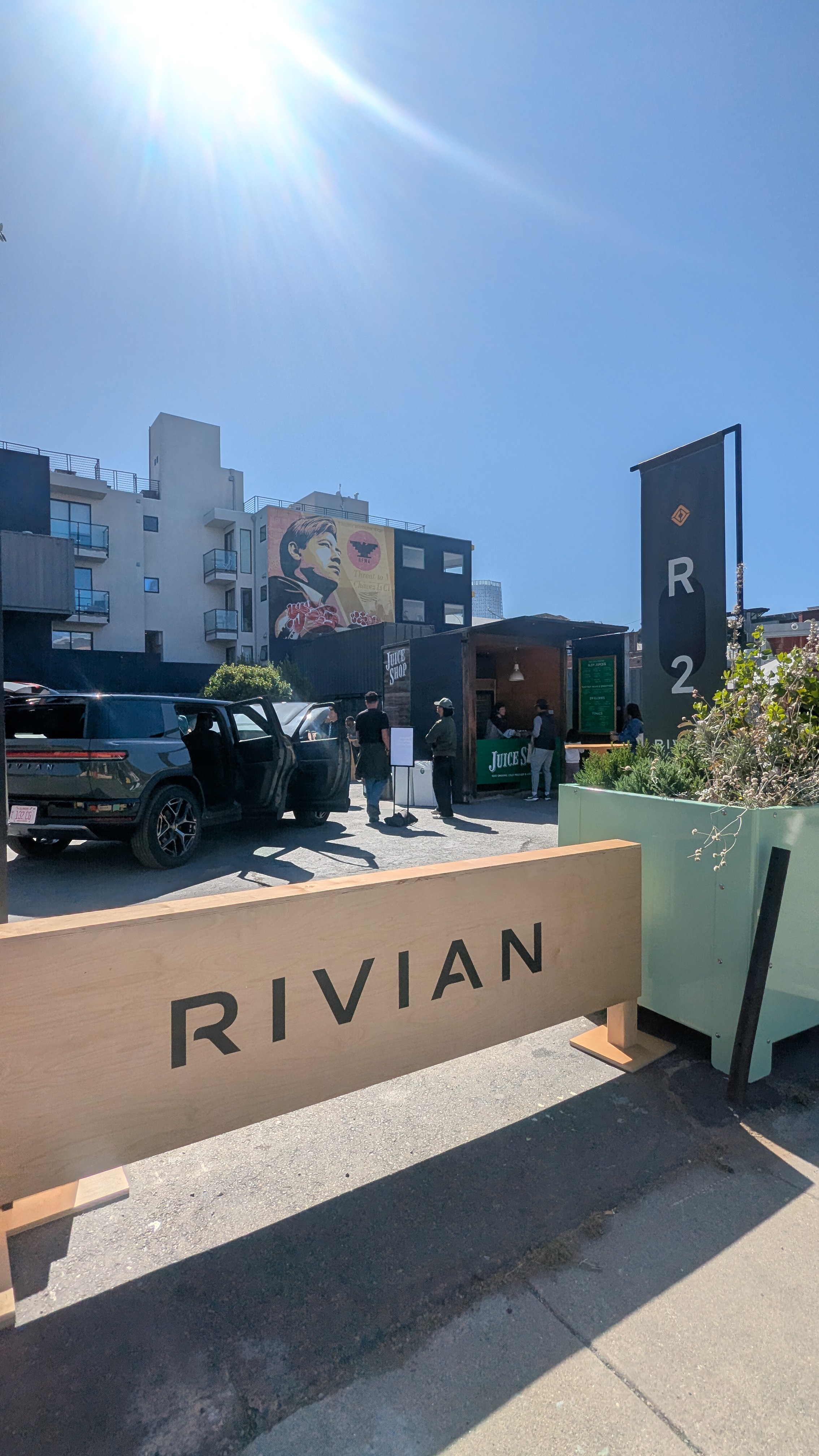 A Rivian demo in Patricia's Green, with a mural of Cesar Chavez on the building behind it